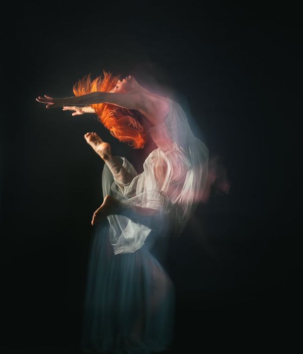 Woman in a dynamic yoga pose against a dark background with ruby light trails.